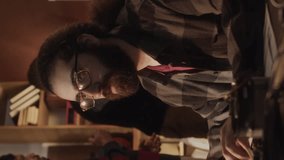 Vertical waist up of long-haired bearded tech lover typing program codes on keyboard while working with other diverse geeks in handmade old-fashioned garage office with warm yellow dimmed light - Powered by Shutterstock - Get 15% off with code: PIKWIZARD15