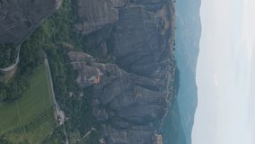 Vertical video. Meteora, Kalabaka, Greece. Meteora - rocks, up to 600 meters high. There are 6 active Greek Orthodox monasteries listed on the UNESCO list, Aerial View, Departure of the camera