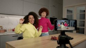 Cheerful playful attractive black female friends having fun and dancing , recording funny video content for social media on mobile phone ,expressing carefree mood and joy indoors.