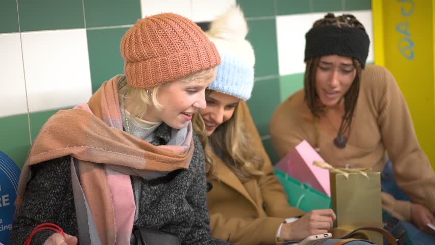 A group of young women share a moment of connection over a smartphone while waiting for the metro, a snapshot of modern urban life and friendship.