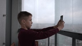 Young handsome boy stands in the balcony and takes a selfie. 11 year old boy with brown hair uses his phone.