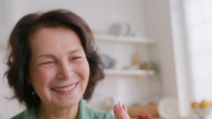 close up view of elderly woman holding pill on hand, takes medicine and drink water. feels good and positive, smiling. old people medicare