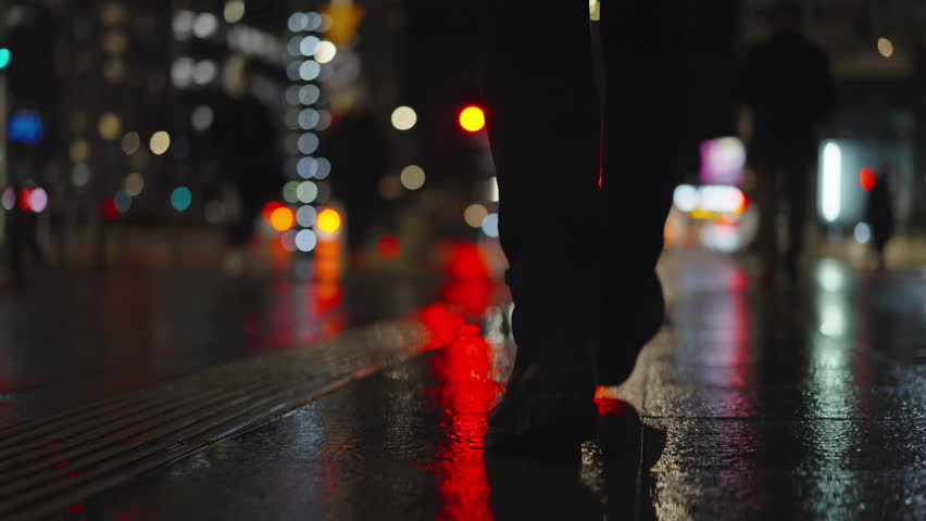 Rear back view male feet steps crossing city street at night. Man wearing dark leather boots goes on sidewalk in city. Low angle legs walking sidewalk, rainy autumn weather, reflected car lights Royalty-Free Stock Footage #3436961271
