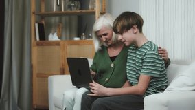Loving grandmother spending time with grandson together at home mature woman granny with kid boy child watching funny video on Internet on laptop, laughing, feeling joy excitement, winning lottery