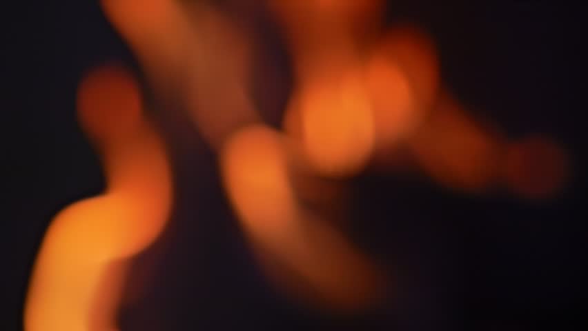 Fire in a fireplace captured out of focus in slow motion, creating an abstract background of black and orange hues.