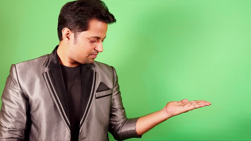 Smiling Man in a formal attire presenting product with an open hand against a green screen background suitable for advertising space Asian male