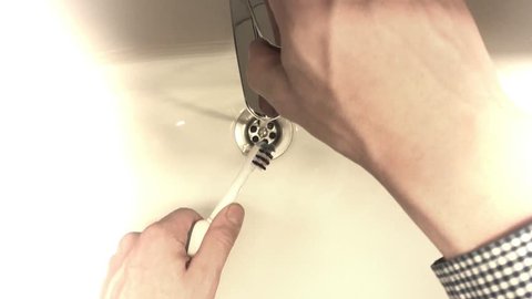 Placing toothpaste on electric toothbrush in bathroom.