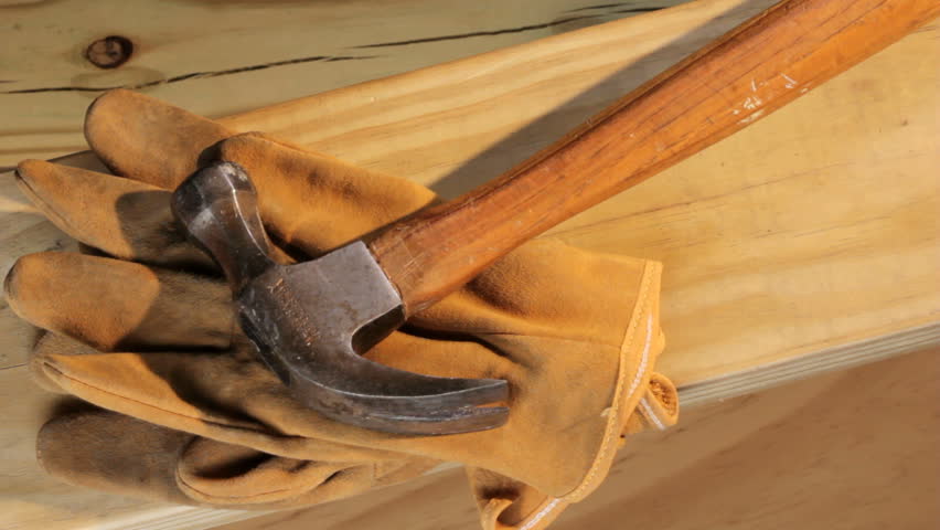 Carpenter puts work gloves, hammer and nails on a  piece of wood