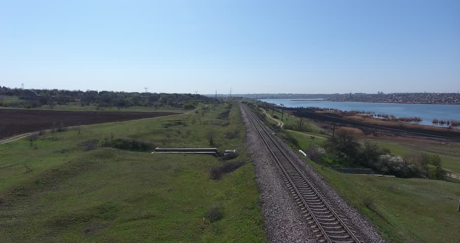 Aerial view. Drone movements along railway track. Steel rails go into distance - nearby are dry reeds and smooth river water