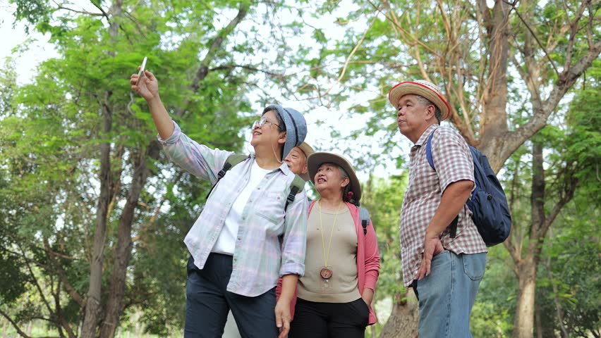 Group of elderly Asians traveling in nature, holding smartphones and taking photos together. Elderly community. Senior tourists. Live happily in retirement