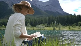 Young woman reading a book by the mountain lake in Canada. People relaxation enjoying outdoor moment concepts. 
