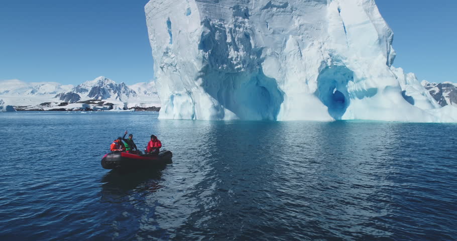People boat tour expedition to Antarctic iceberg. Antarctica travel and exploration. Arctic winter glacier drift ocean. Pristine South Pole landscape, sunny day. Aerial drone flight panoramic zoom out