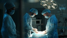 Diverse team of professional male surgeons and female nurse performs invasive surgery on patient in hospital. African-American assistant helps head surgeon apply sutures. Shooting in slow motion. - Powered by Shutterstock - Get 15% off with code: PIKWIZARD15
