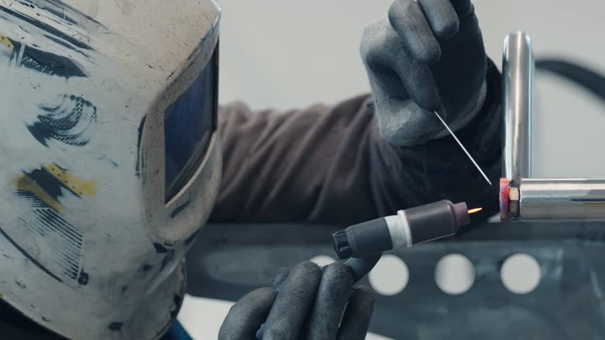a man wearing a welding mask is welding a pipe, stainless steel