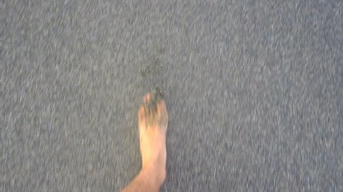 Legs of a tanned Caucasian man walking barefoot on a sandy beach among the sea surfs. First person POV.