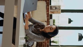 Vertical video Relaxed cheerful remote worker listening to music on headphones while working from home. Smiling freelancer enjoying herself, typing on laptop in stylish personal office, camera A - Powered by Shutterstock - Get 15% off with code: PIKWIZARD15