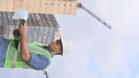 Vertical video of latin construction worker man looking documents in construction site in sunny day