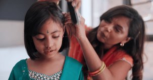 Indian mother brushing child hair in living room of family home with traditional outfit. Love, care and young mom with girl kid getting ready with hairstyle in culture clothes or fashion at house.