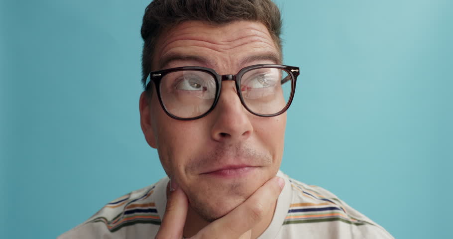 Thinking, face and man with glasses in studio for brainstorming, problem solving or idea on blue background. Why, questions or model portrait with plan emoji for solution, memory or guess expression