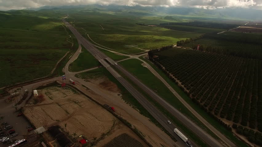 Aerial Tilt Up Shot Of Vehicles Moving On Roads By Green Plants Under Cloudy Sky - Bakersfield, California