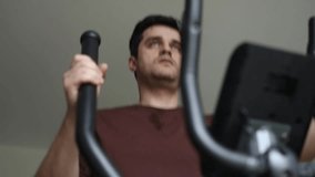 middle age man doing exercises on elliptical trainer in living room at home