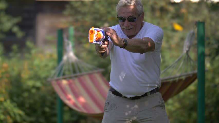 Senior man playing with a toy gun fight on nature, slow motion