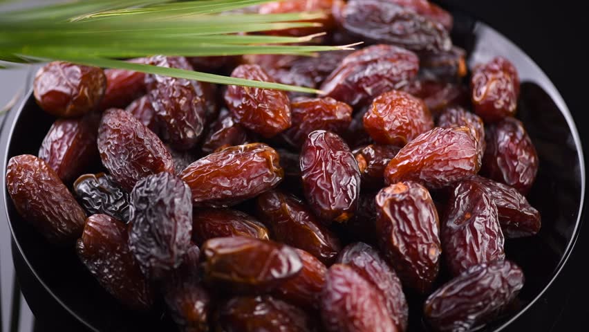 Dates fruit. Date fruits rotating on black background. Big plate full of Arabian Medjool dates with leaf close up. Tasty healthy vegan food