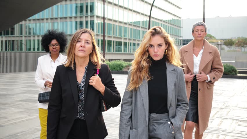 Slow motion fotage of a group of real executive businesswomen walking and staring front with serious and proud expression at workplace. Toughtful and succesful business females team looking at camera