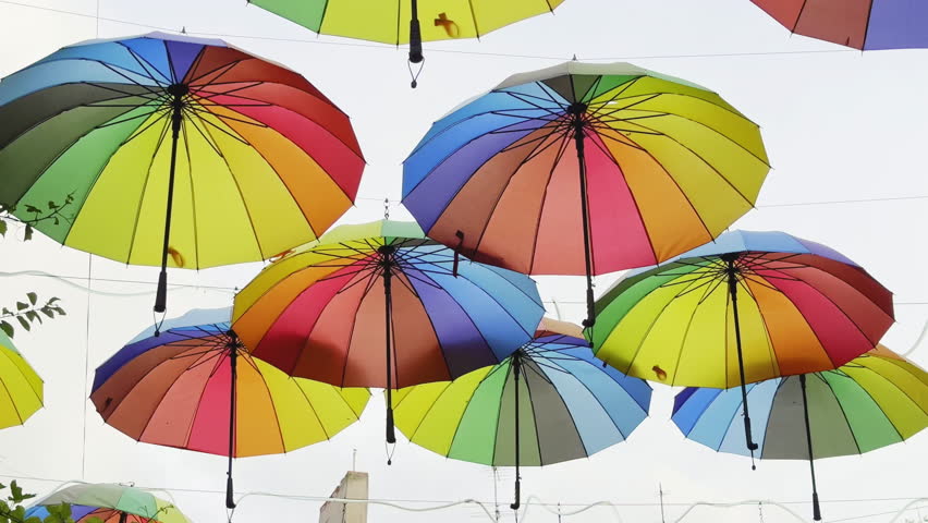 Lot multi-colored rainbow umbrellas hang above city street. Fun lgbt coming out concept. Colorful gay symbol. Urban art overhead decoration. Many vivid csd umbrella sway open air. Blue sky background.