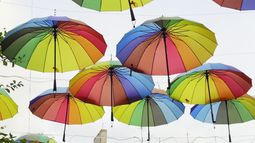 Lot multi-colored rainbow umbrellas hang above city street. Fun lgbt coming out concept. Colorful gay symbol. Urban art overhead decoration. Many vivid csd umbrella sway open air. Blue sky background.