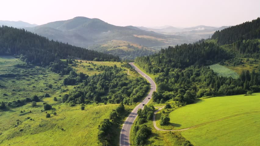 Flight over the summer mountains with mountain road serpentine, green meadows and forest. Ukraine, Carpathian mountains. Footage from drone. UHD 4k video