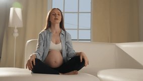 Pregnant woman doing meditating at home. Pregnant female doing yoga practice stretching with online lesson video training at home. Mother and child health relax and meditation exercise concept.