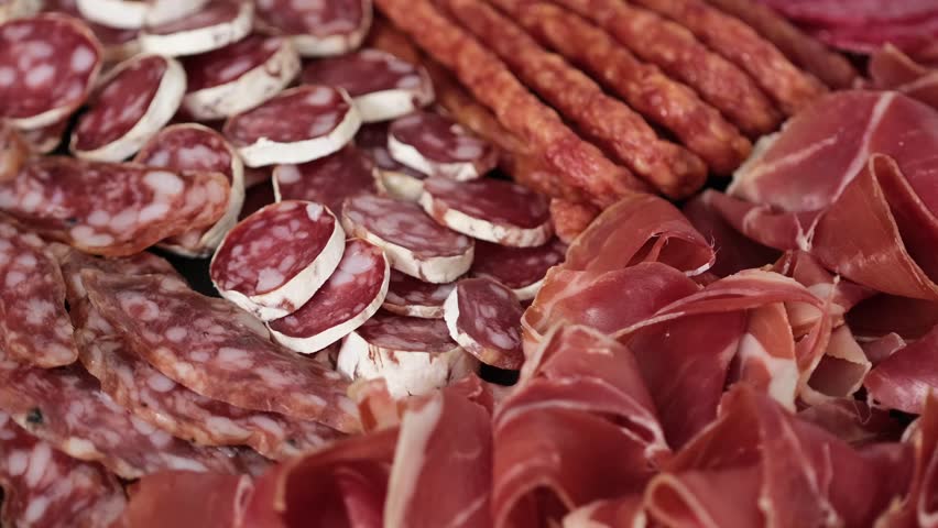 Meat plate with assortment of various tasty Spanish, french or Italian appetizers - sliced prosciutto, sausage, ham, boiled pork, balyk, jamon, sandwich, cheese, salami. Meat platter rotating