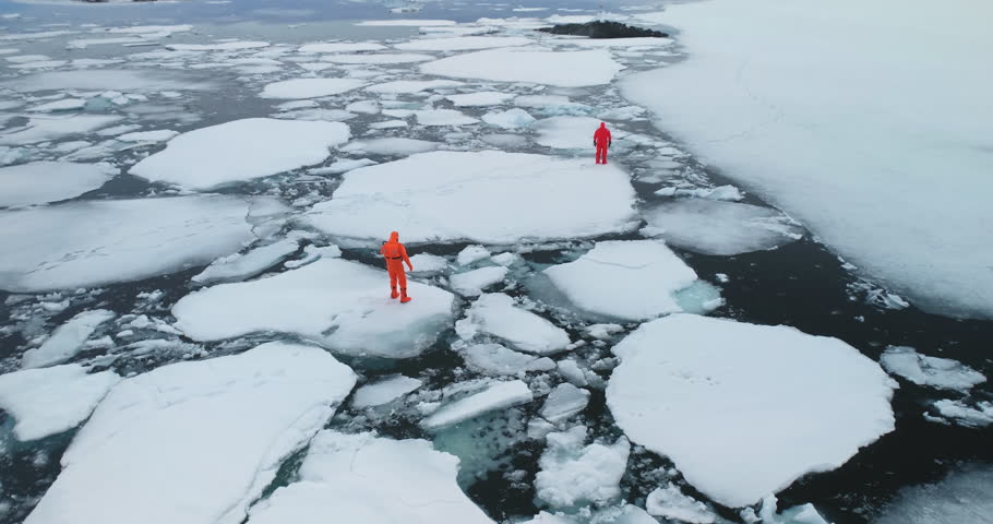 People in immersion suits on melted arctic ice. Two man in orange wetsuits stuck in polar trap try to run melting winter ocean cold water. Explore global climate warming melt glaciers. Aerial panorama