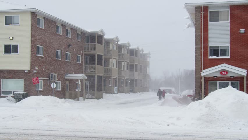 Blizzard, strong wind, wet snow, silhouettes of people are blurred against background of houses, they are trying to hide from weather, overcoming all difficulties harsh climate. Dartmouth, Canada.