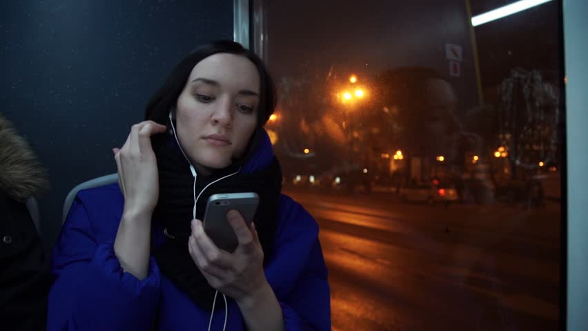 Young cute girl using smart phone listening music with headphones smiling during bus ride in evening in city. Car traffic on background. Slow motion Royalty-Free Stock Footage #34379056