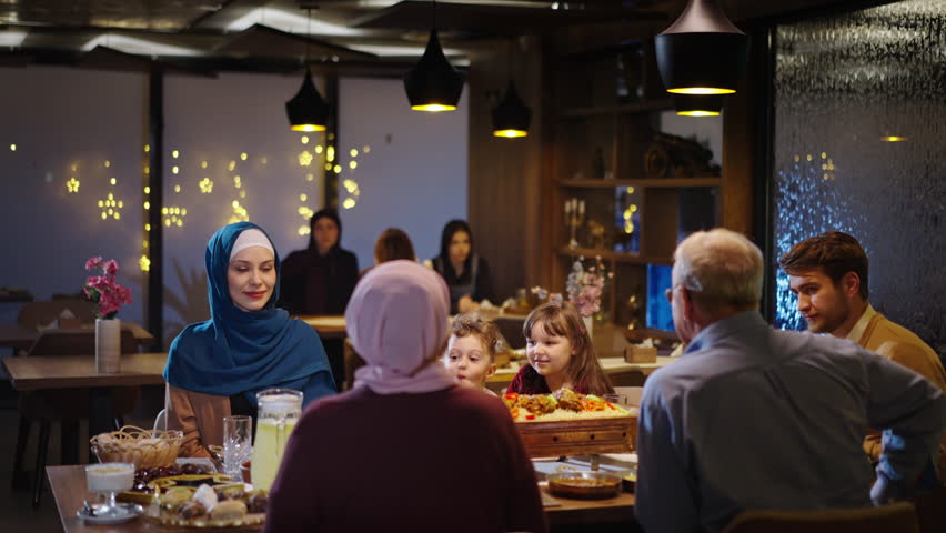 Muslim Family Sitting Around the Restaurant Table in Ramadan or on Eid. Crescent and Star Motifs. Meat and Sweets on the Table Royalty-Free Stock Footage #3437923835