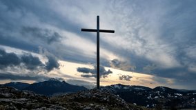 Christian cross on a rock in a mountain landscape, Dramatic clouds over the silhouette of the mountains in winter, Timelapse