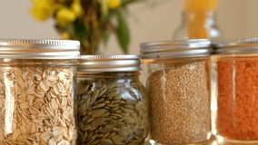 Hand held video showing a collection of glass jars in a sunny window. Close up showing the texture of the seeds and grains representing a sustainable pantry in a zero waste kitchen.