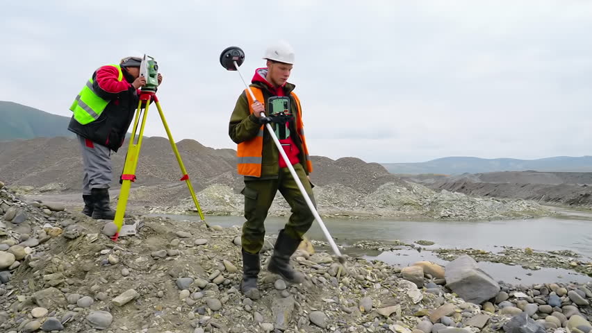 Surveyor Specialist Measures Gold Mine Area By Theodolite Equipment. Young Surveyor With Prism Pole Equipment Measuring Elevation Of Gold Mine Ground. Two Male Surveyors Working At Gold Mining Site Royalty-Free Stock Footage #3438041755