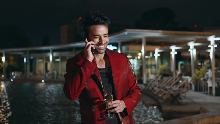 Luxurious businessman ending call celebrating at night party on poolside. Glamorous spanish man talking smartphone late evening outdoors closeup. Handsome happy guy in red suit holding champagne glass Royalty-Free Stock Footage #3438043919