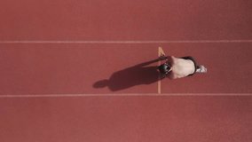 Bird's eye view of a runner on an athletics track. From short shot to large wide shot of the whole track and rails. Top view in vertical drone video. Concept of sport and self-improvement.