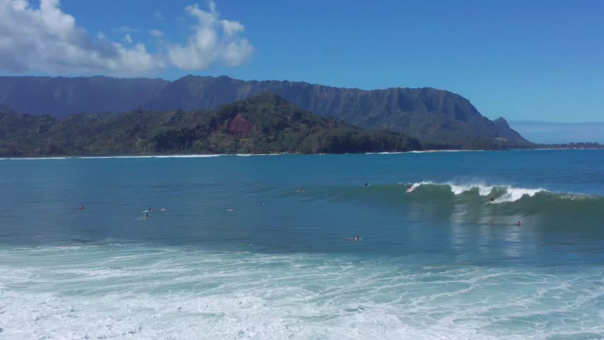 Hawaii Hanalei Bay surfers riding big waves. Sunny day in Kauai aerial drone video. Ocean lifestyle, and extreme sports