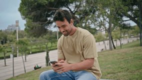 Happy man dial phone number relaxing at street bench close up. Smiling handsome guy start cellphone call sitting green park at weekend. Cheerful latin hipster talk smartphone at urban garden greenery. - Powered by Shutterstock - Get 15% off with code: PIKWIZARD15