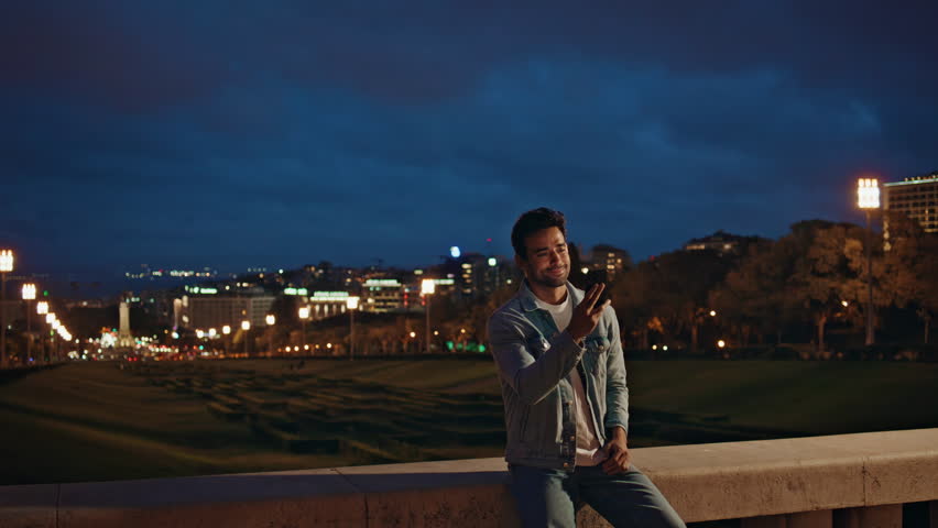 Man waving hand to cellphone web camera at night city. Hispanic guy talking at mobile phone video call showing evening town views. Happy tourist enjoy online friendly meeting by smartphone outdoors. Royalty-Free Stock Footage #3438151453