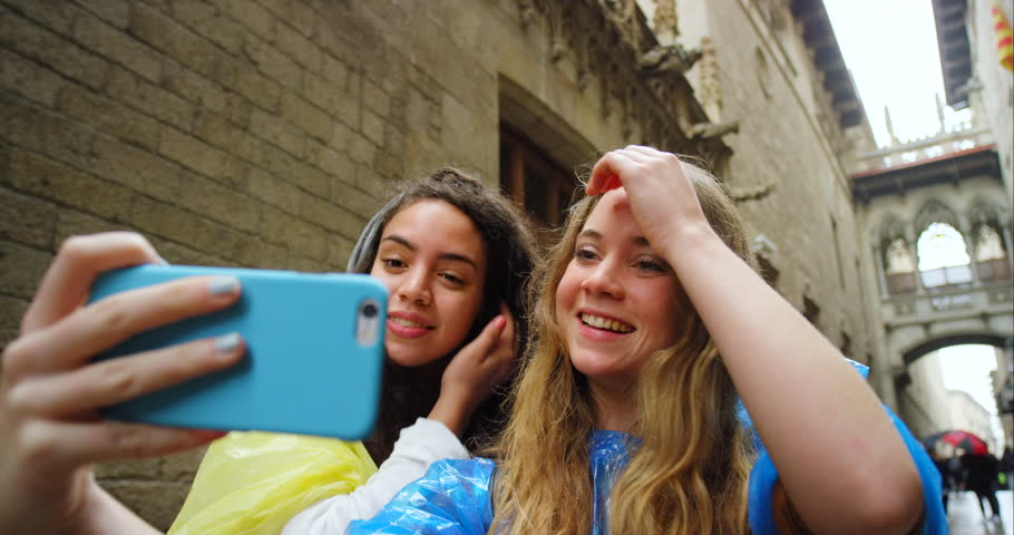 Friends, women and selfie in street, rain and funny face with smile, peace sign and excited for live stream. Group, gen z girl and people with photography, post and social network in Barcelona