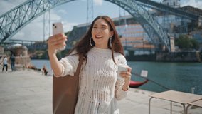 Cheerful blogger holding smartphone recording video at river promenade closeup. Happy asian lady using modern cellphone to take picture cityscape. Attractive girl tourist enjoy photographing outdoors 