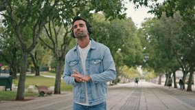 Latin hipster listening music by wireless earphones walking beautiful green park. Casual hispanic man enjoy rhythmic sound in headphones at relaxed weekend stroll. Young melomaniac going on alley. - Powered by Shutterstock - Get 15% off with code: PIKWIZARD15