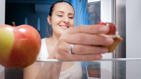 4k video of young woman taking sweet cake from fridge at kitchen. Concept of unhealthy food and dieting