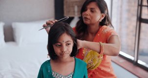 Indian mother brushing kid hair in living room of family home with traditional outfit. Love, care and young mom with girl child getting ready with hairstyle in culture clothes or fashion at house.